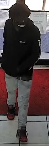 Image of first suspect at location dressed in dark hoodie and light gray jeans with red and black shoes. 